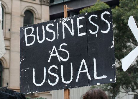 Schwarzes Demo-Schild mit der Aufschrift "Business as Usual".