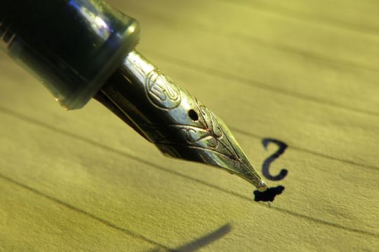 Ein Füller schreibt ein Fragezeichen auf ein Stück Papier. 