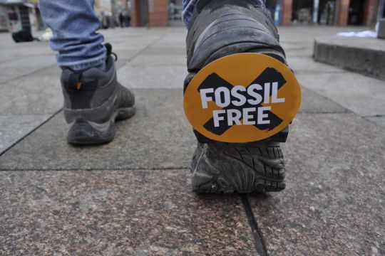 Das Bild zeigt einen Aktivisten der Divestment Bewegung mit Schuhen, die "Fossil free"-Aufkleber unter den Sohlen haben.