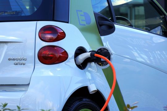 Ein Elektroauto wird aufgeladen - man sieht nur den hinteren rechten Teil des weißen Kleinwagens sowie das orangefarbene Stromkabel.