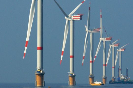 Eine Reihe Windräder auf See, dazwischen ein Motorboot und hinten eine schwimmende Bauplattform.