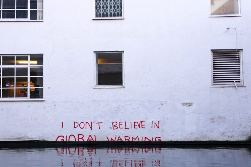 Graffiti an einer Hauswand, wo das Wasser schon die Hälfte der unteren Zeile erreicht hat. der englische Text bedeutet: Ich glaube nicht an die globale Erwärmung.