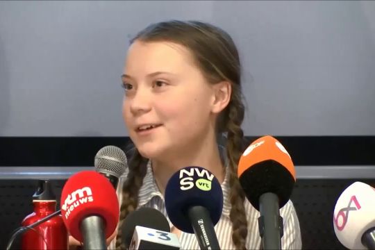 Greta Thunberg lächelt hinter einer Ansammlung von Mikrofonen.