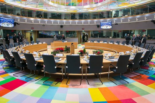 Runde Stuhl-Anordnung im Sitzungssaal für die EU-Gipfel, ein Kreis aus dezenten bis kräftigen farbigen Rechtecken an Boden und Decke.