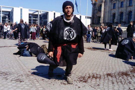 Mann in schwarzem Umhang mit Extinction-Rebellion-Symbol (eine Sanduhr von einem Kreis umschlossen)