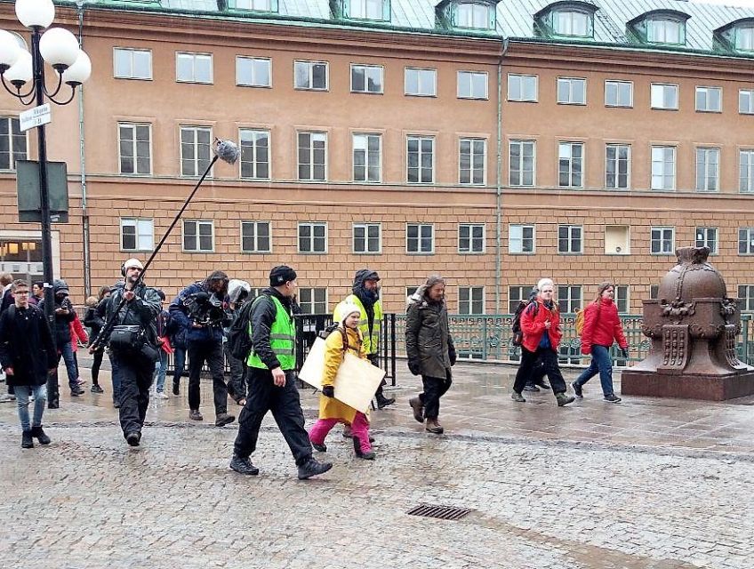 Greta Thunberg geht mit einem großen Schild bei regnerischem Wetter die Straße entlang.