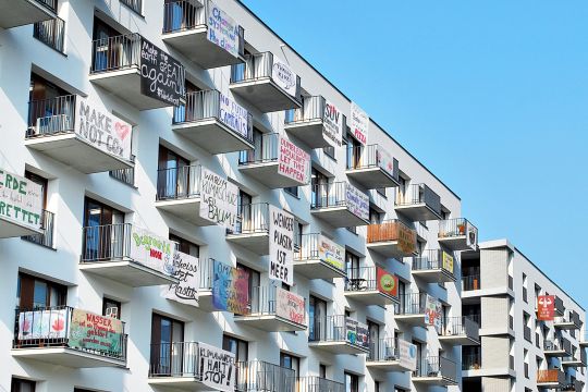 Zahlreiche Balkons an einem mehrstöckigen neuen Wohnhaus, an jedem ein Transparent mit einem Umweltschutz-Slogan.