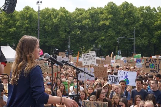 Luisa Neubauer spricht auf einer Bühne, im Hintergrund Demonstrierende.