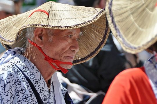 Mann mit ernstem Gesicht, Kimono und traditionellem Sonnenhut aus Stroh