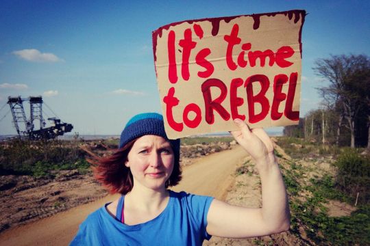 Kathrin Henneberger an Tagebau-Kante hält Schild mit roter Aufschrift 