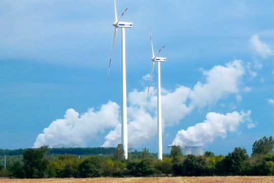 Zwei Windräder vor fast blauem Himmel, im Hintergrund dampfende Kühltürme des Kraftwerks Jänschwalde.