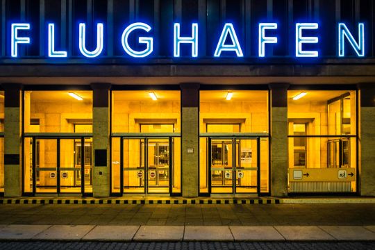 Nächtlich beleuchteter Eingang mit dem Neonschriftzug