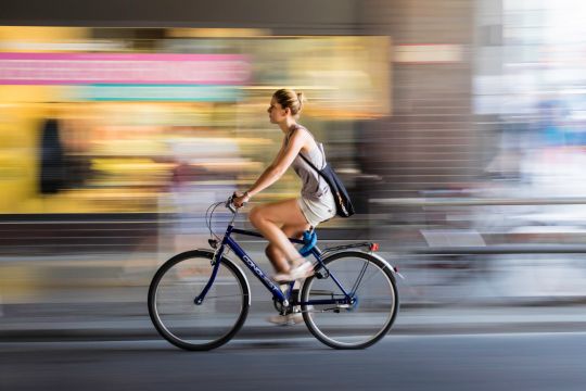 Radfahrerin fährt schnell an nur unscharf zu erkennendem Schaufenster vorbei.