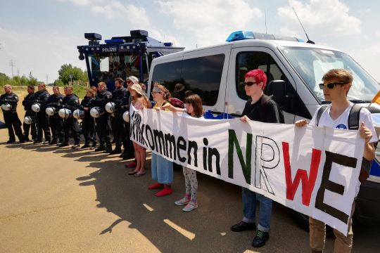 Klimaaktivsten mit Protesttransparent, daneben Polizei