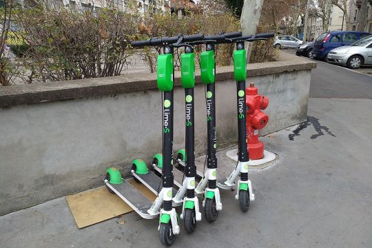 Vier grün-schwarze Elektro-Tretroller stehen an einer Straßenecke in Lyon.