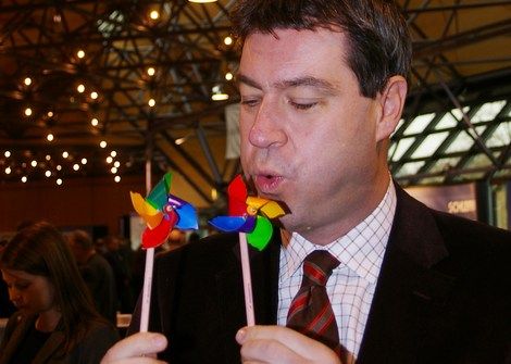 Markus Söder bläst zwei bunte Kinder-Windräder an.