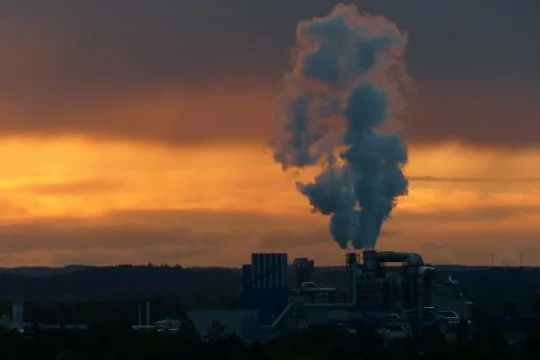 Aus einer Industrieanlage steigt Rauch in den bräunlich-gelben Abendhimmel.