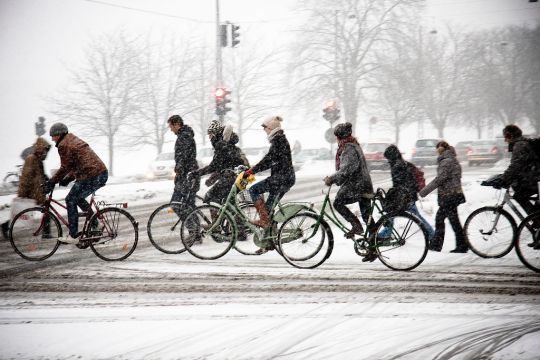 Radfahrer und Fußgänger überqueren eine winterlich verschneite Straße.