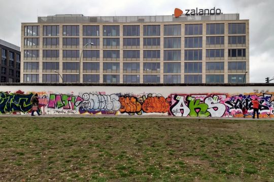 quaderförmiges Gebäude mit Zalando-Logo, davor Berliner East Side Gallery und Wiese