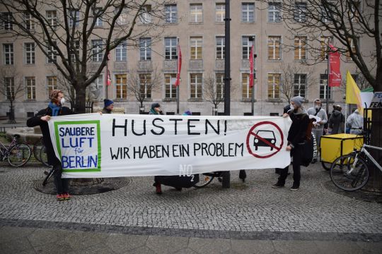 Demonstranten halten ein Transparent mit einem durchgestrichenen Auto und der Aufschrift: "Husten! Wir haben ein Problem! – Saubere Luft für Berlin".