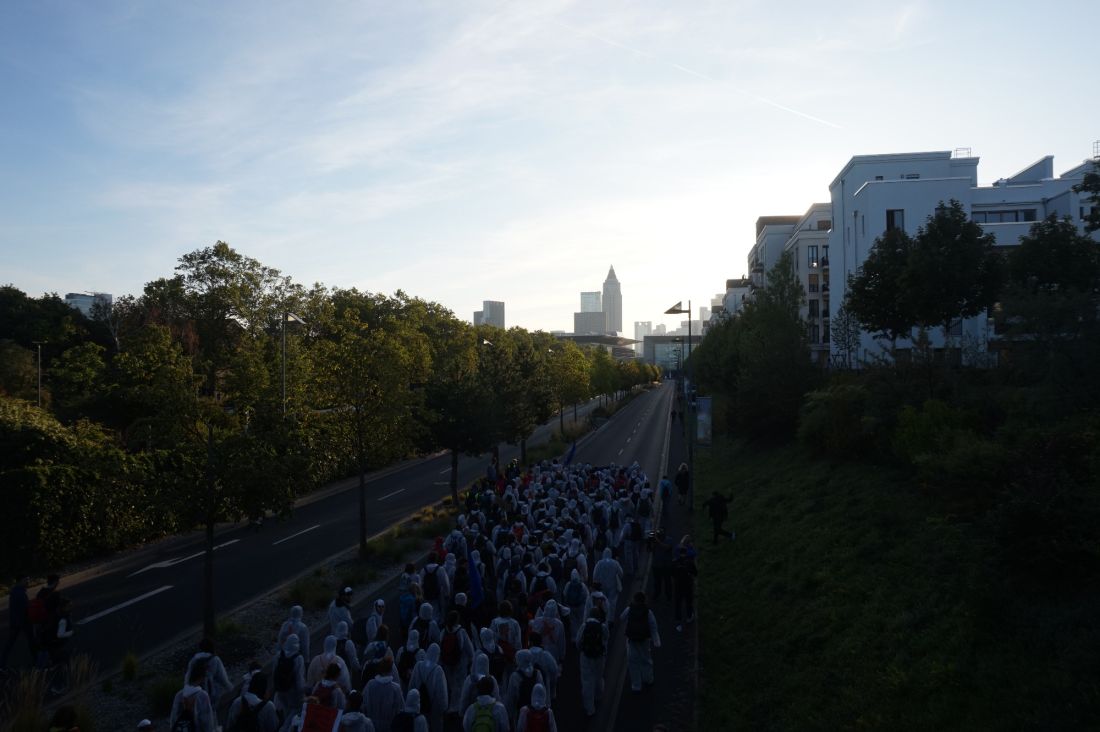 Eine große Gruppe Menschen geht auf einer Straße auf einen Gebäudekomplex zu.