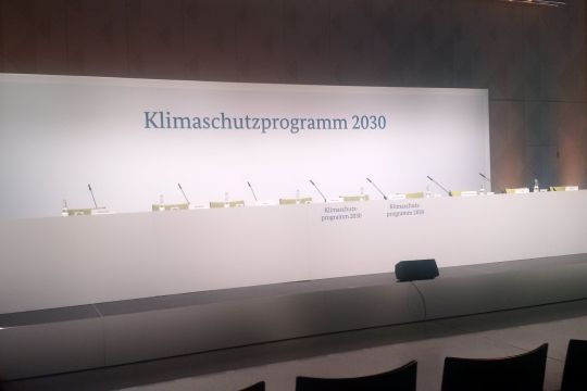 Leere Stühle auf einem Podium mit der Aufschrift "Klimaschutzprogramm 2030".