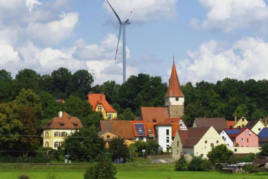 Ansicht eines Dorfes mit Kirche, Windrad und Solardächern.