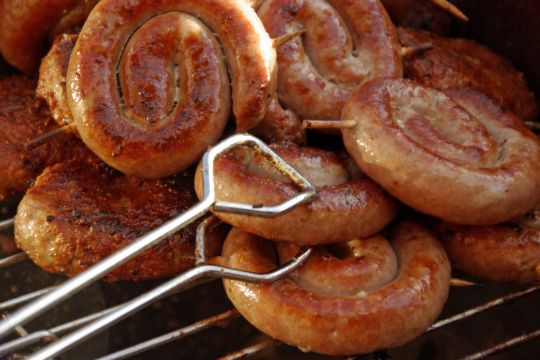 Einige gerollte Grillwürstchen liegen auf einem Grill.