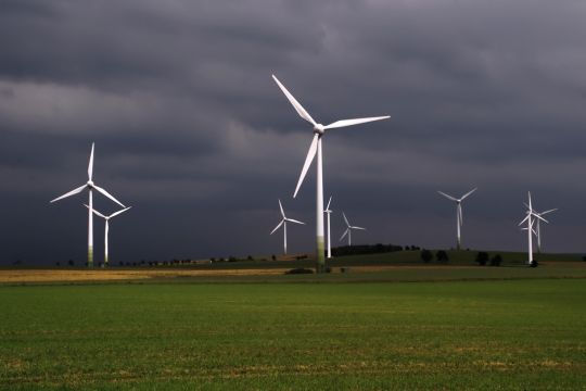 Dunkle Wolken über einigen Windrädern auf einem Feld.