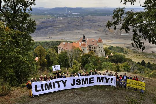 Aktivisten mit einem Banner stehen vor einem Brankohletagebau, an desssen Rand eine Kirche steht. 