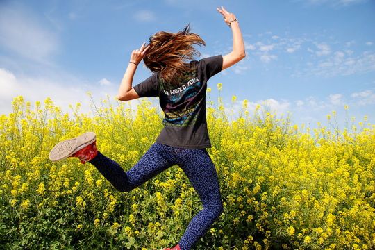 Vor einem blühenden Feld ist ein junger Mensch zu sehen, der einen Freudensprung macht