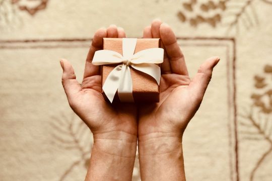 Ein sehr kleines Geschenkpaket liegt auf zwei geöffneten Händen.
