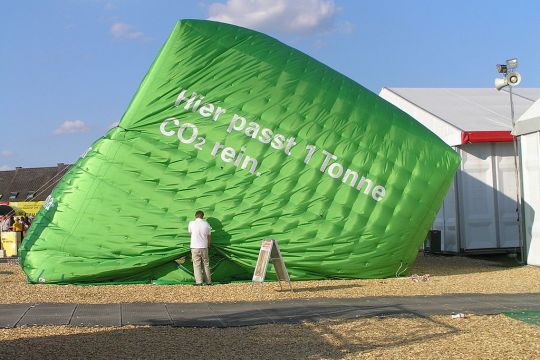 Ein grüner würfelförmiger Ballon ist zu zwei Dritteln mit Luft gefüllt und trägt die Aufschrift: "Hier passt eine Tonne CO2 rein."