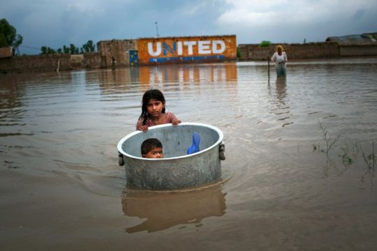 Ein Mädchen schleppt ihren kleinen Bruder in einer Wanne über die überfluteten Straßen in einem pakistanischen Dorf