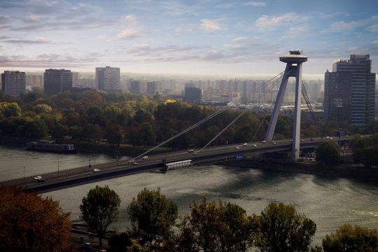 Große Brücke und Grünstreifen an Fluss, dahinter eckige Hochhäuser in Bratislava