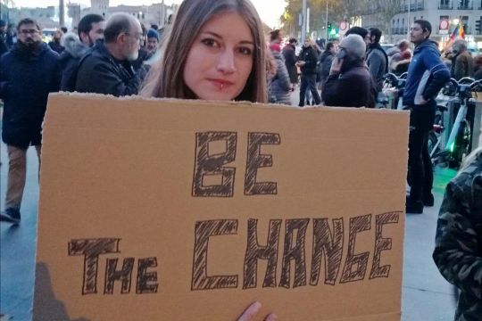 Junge Frau mit Schild "Be the change"