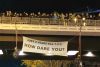 Mit Menschen gefüllte Brücke, zwei Menschen davon abgeseilt, dabei ein Banner "Just 8 years to 1,5°. How dare you?"