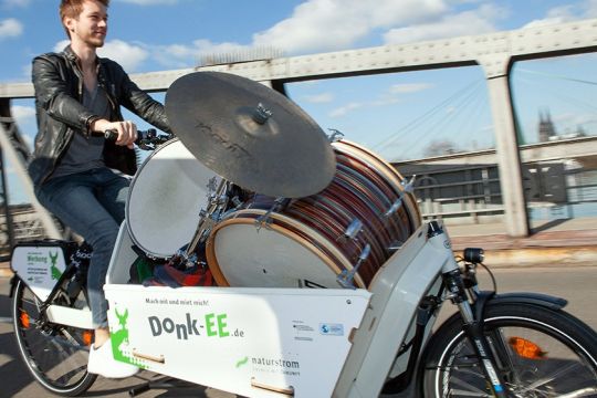 Mann fährt mit einem Lastenrad, in dem er ein Schlagzeug transportiert.