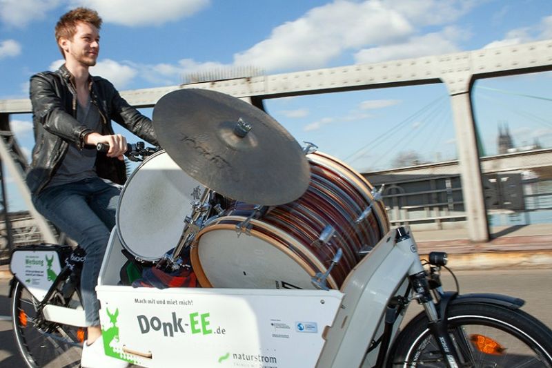 Mann fährt mit einem Lastenrad, in dem er ein Schlagzeug transportiert.