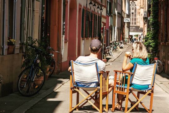 In einer Gasse in Heidelberg sitzt ein Paar auf Holz-Klappstühlen in der Sonne.