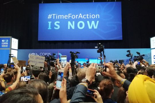Handgemenge bei einer Protestaktion auf dem Klimagipfel in Madrid, man sieht vor allem hochgehaltene Fotohandys und das Konferenzmotto "Time for action is now".. 