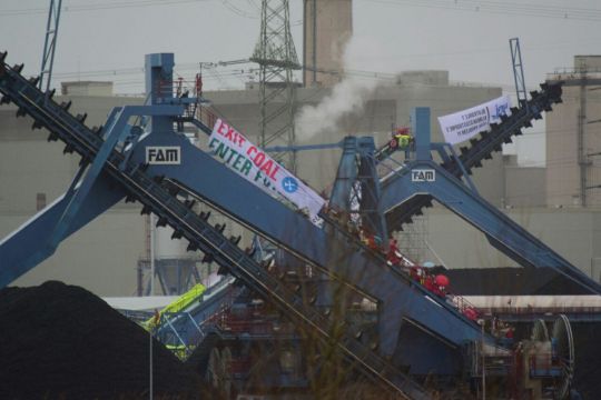 Menschen und Banner "Exit coal, enter future" auf blauem Kran vor grauen Gebäuden und Qualm
