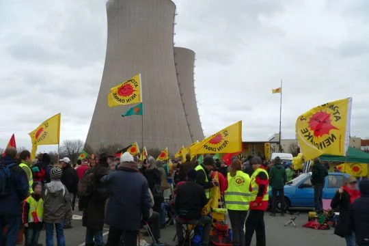 Menschen stehen vor den beiden Kühltürmen des AKW Grohnde und schwenken gelbe Fahnen mit der roten Anti-Atom-Sonne.