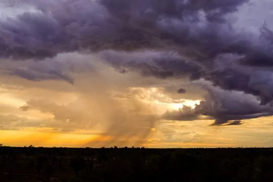 In einer ebenen Wüstenlandschaft ziehen in der Dämmerung Regenwolken, am Horizont regnet es.