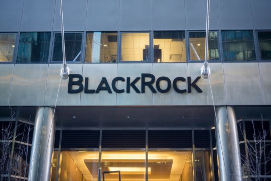 Schwarzer Schriftzug "Blackrock" über dem von innen mild beleuchteten Eingangsportal des modernen Gebäudes der Firmenzentrale in New York City.