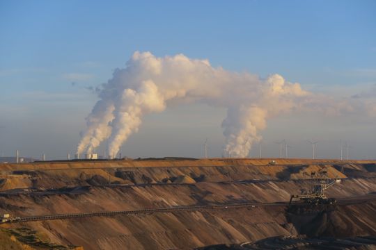 Der Braunkohletagebau Garzweiler, weit im Hintergrund dampfen Kohlekraftwerke gegen den blauen Himmel.