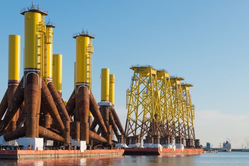 Jeweils mehrere dreibeinige Jacket-Gründungen für Offshore-Windräder stehen auf einigen schwimmenden Transportuntersätzen.