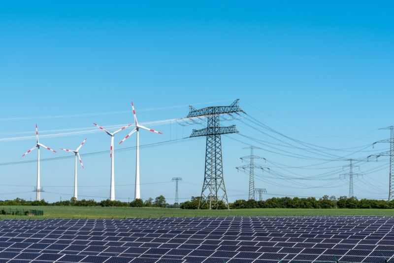 Ein Windpark, eine Solar-Freiflächenanlage und Stromleitungen auf einem Feld.