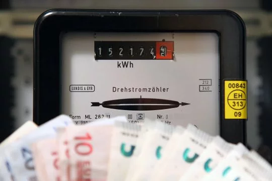 Aufgefächerte Geldscheine vor einem Stromzähler.