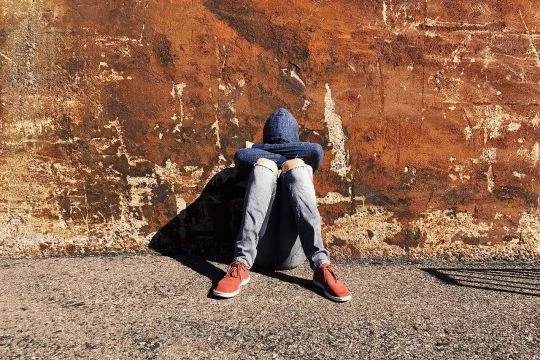 Junge Person sitzt auf dem Boden, den Kopf auf die Knie gesenkt